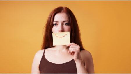 woman holding fake smile in front of her face