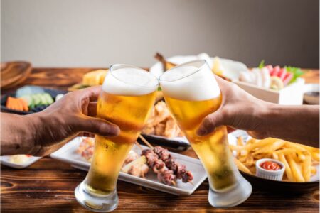 two people clink their beeg mugs togther in front of a table full of food