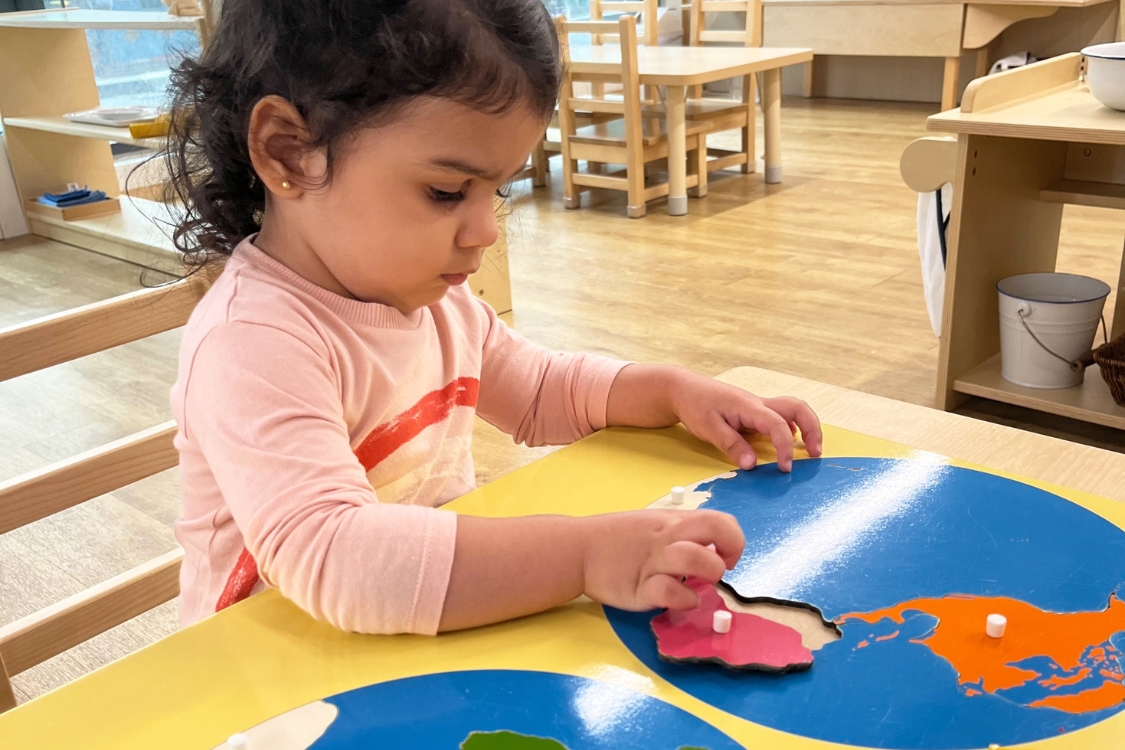 a young child sitting at a table completing a map of the world puzzle