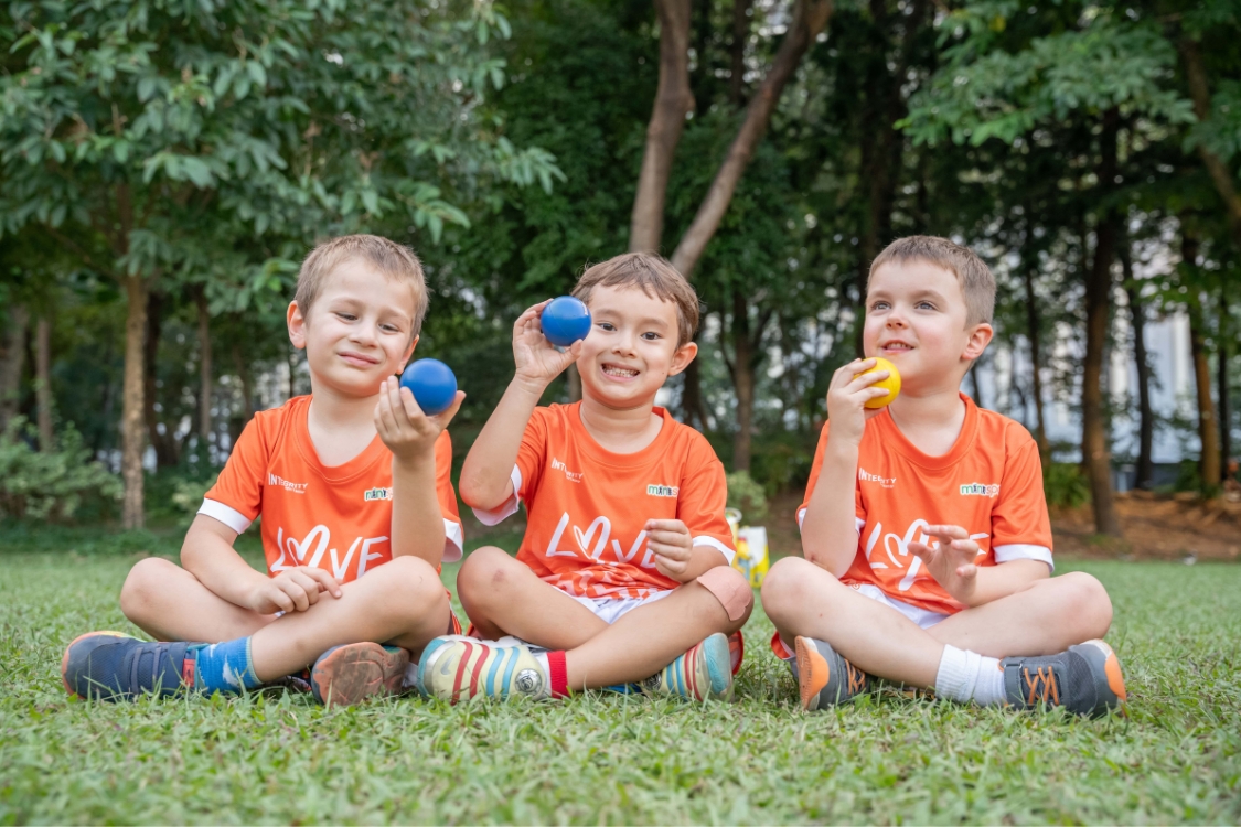 three boys sitting on a grassy lawn